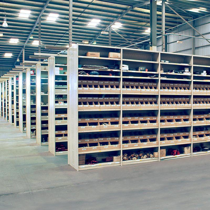 Multiple bays of rolled upright shelving installed in a warehouse, showing high-density storage layout., Single bay of rolled upright shelving, highlighting the compact and sturdy design., Close-up view of the metal shelves on a rolled upright shelving unit, showing smooth finish and load capacity., Detailed view of a rolled upright shelving post, showing vertical perforations for shelf adjustment., Close-up of a metal shelf clip used to secure shelves to the upright frame., Single rolled steel shelf for upright shelving, showcasing reinforced construction., Side angle of a rolled upright shelving upright, displaying its structural profile and strength., Shelf clip inserted into the upright post, demonstrating tool-free shelf installation., Top view of a shelf on a rolled upright system, highlighting depth and surface texture.